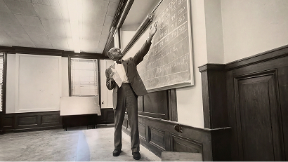 David Blackwell teaching at a chalkboard in a lecture hall, holding papers while writing